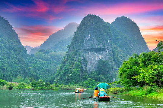 Ninh Binh, Vietnam - April 5th, 2024: Tourists float by boat on the river of the Tam Coc National Park Sightseeing tour to grottoes with sunset sky, Ninh Binh, Vietnam.