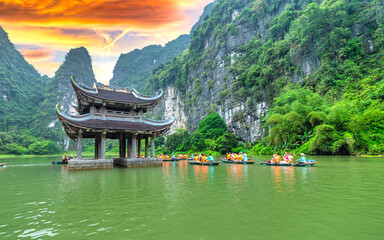 Obraz premium Ninh Binh, Vietnam - April 5th, 2024: Tourists float by boat on the river of the Tam Coc National Park Sightseeing tour to grottoes with sunset sky, Ninh Binh, Vietnam.