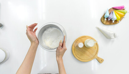 Hand sifting flour in a kitchen with baking ingredient and colorful icing on the side. Top view