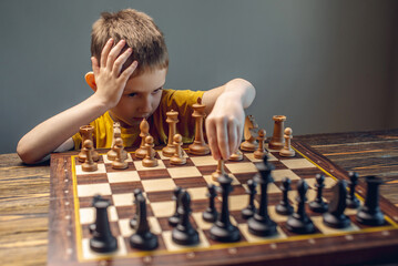 The child is a boy playing chess alone at the board. The process of thinking about a move to...