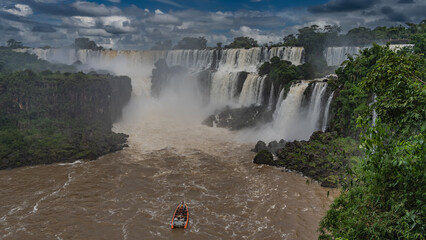 A tourist boat rushes along the bed of a stormy river to a waterfall. The streams collapse in...
