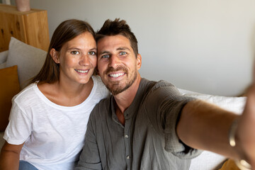 Fototapeta premium Young couple taking selfie relaxing sitting on the sofa looking at camera.