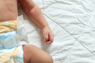 Newborn Baby Hand And Leg In Diaper, Lying On White Bed, Top View, Copy Space