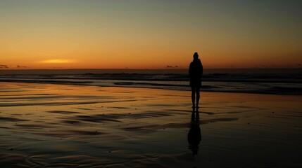Fototapeta premium A person stands on a beach at sunset. The sky is orange and the water is calm. The person is alone and looking out at the ocean