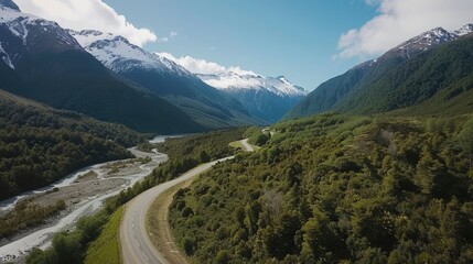 A mountain range with a winding road that runs through it. The road is surrounded by lush green trees and a river. The scene is peaceful and serene, with the mountains in the background