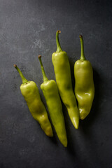 banana peppers on black textured background, long curved shape with mild heat and tangy sweet...
