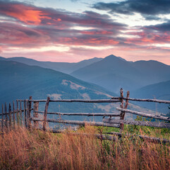 Wooden fence on mountain pasture at sunrise. Splendid summer view of mountain village. Attractive...