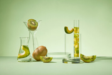 Various types of laboratory glassware containing kiwi, avocado and transparent liquid over green...