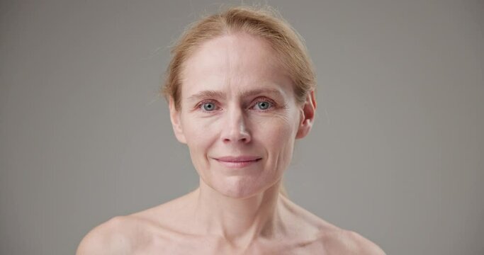 Anti age, Beauty, health and dry skin care concept - beautiful middle-aged mature Caucasian woman in her 50s touching her face skin and looking at the camera with a slight smile