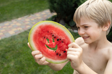 boy happily eats a watermelon, carving a smile in a round piece of watermelon. Hello summer, good mood, delicious vitamin food. The joy of childhood