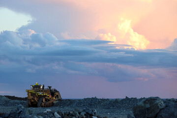 Dozer, bulldozer, crawler working at a mine, sunset, thunderstorm clouds, dramatic colorful sky,...