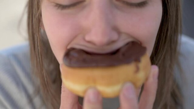 A close-up shot of a woman enjoying a chocolate-covered donut, focusing on the mouth and donut, highlighting the pleasure of eating sweet treats.