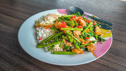 Fried Morning Glory with Crispy Pork or meal with Thai style fried egg with rice in white dish on wooden table. Thai style food.