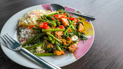 Fried Morning Glory with Crispy Pork or meal with Thai style fried egg with rice in white dish on wooden table. Thai style food.