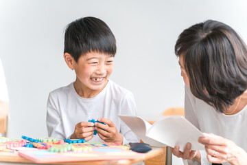 学校の教室でアルファベットのおもちゃを使って英語を勉強する小学生低学年の男の子と女性教師
