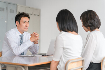 Obraz premium 三者面談で厳しい話をする男性担任教師・先生と落ち込む生徒と保護者 