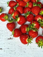 Vertical close-up shot of ripe, juicy, fresh strawberries. Red strawberries on a light wooden table, top view. 