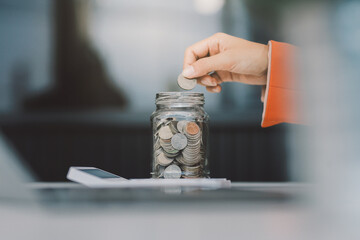 Beautiful Asian businesswoman insert coins in a pin piggy bank on the table. saving money,...