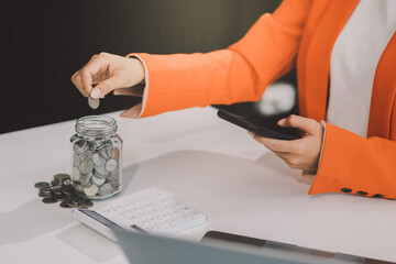 Beautiful Asian businesswoman insert coins in a pin piggy bank on the table. saving money,...