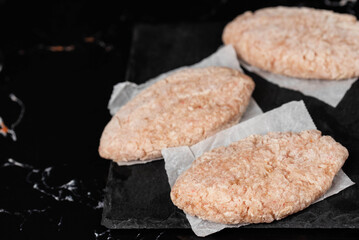 Frozen chicken meat cutlets on dark black background, semi-finished, ready for cooking. Convenience and homemade frozen healthy meals.