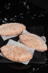 Frozen chicken meat cutlets on dark black background, semi-finished, ready for cooking. Convenience and homemade frozen healthy meals.