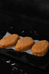 Frozen fish cutlets on dark black background, semi-finished, ready for cooking. Convenience and homemade frozen healthy meals.