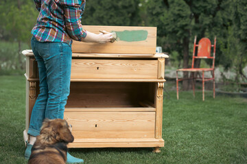Woman painting a wooden furniture while sitting with her dog in the garden. DIY concept.