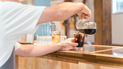 カフェ・飲食店のカウンターでコーヒをグラスに注ぐ店員・キッチンスタッフの男性
