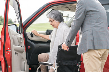 自動車から降りて車椅子に乗る高齢者女性と介助する男性（移乗）

