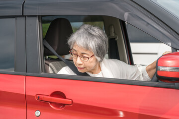 駐車場で自動車の窓を開けてバックする高齢者ドライバーの女性
