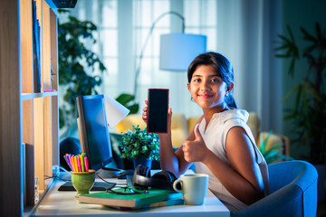 Indian asian teenage school girl studying online at home using smartphone and computer