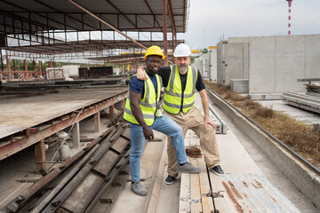 Portrait happy caucasian engineer man hug with happy African American engineer man at precast cement outdoor factory	