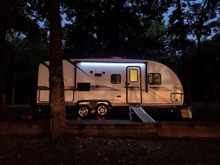 Illuminated camper trailer parked in forest at night.