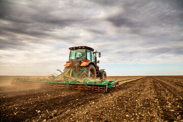 Powerful tractor tills the soil, preparing the land for planting under a dramatic sky