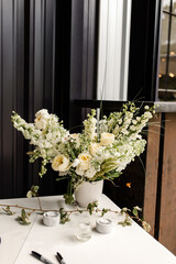 White floral arrangement in a vase on a table with candles and pens