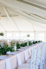 Elegant white wedding reception tent with long tables and greenery