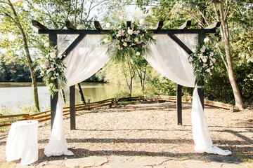 Outdoor wedding arch with white drapery and florals by lake