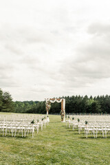 Outdoor wedding ceremony with floral arch and rows of white chairs=