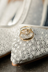Close-up of gold wedding rings on white, beaded bridal shoes