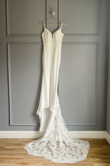 White wedding dress with lace details hanging on a gray paneled wall