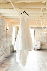 Elegant white wedding dress hanging in a rustic, industrial-style room