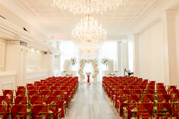 Wedding ceremony with red chairs, white florals, and chandeliers
