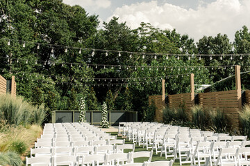 Outdoor wedding aisle with white chairs under lights