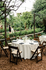 Outdoor garden reception setup with round tables and wooden chairs