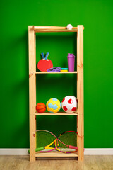 Shelves with different sports equipment against green wall