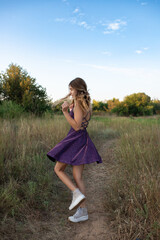 Sixteen-year-old girl in a purple dress twirling gleefully in a field