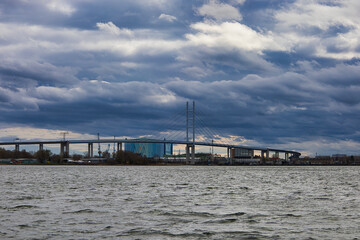 Obraz premium Blick vom Wasser auf die Rügenbrücke, den Strelasund, moderne Schrägseilbrücke als Verbindung zur Insel Rügen unter dramatischem Wolkenhimmel, Hansestadt Stralsund, Mecklenburg-Vorpommern, Deutschland