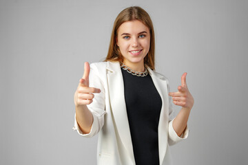 Young Woman in White Blazer Pointing at You Against a Grey Background