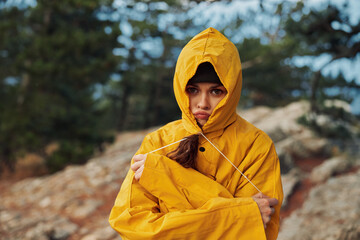 A young woman in a yellow raincoat standing on a rocky hill with trees in the background during a nature excursion