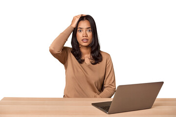 Filipino woman at desk with laptop being shocked, she has remembered important meeting.